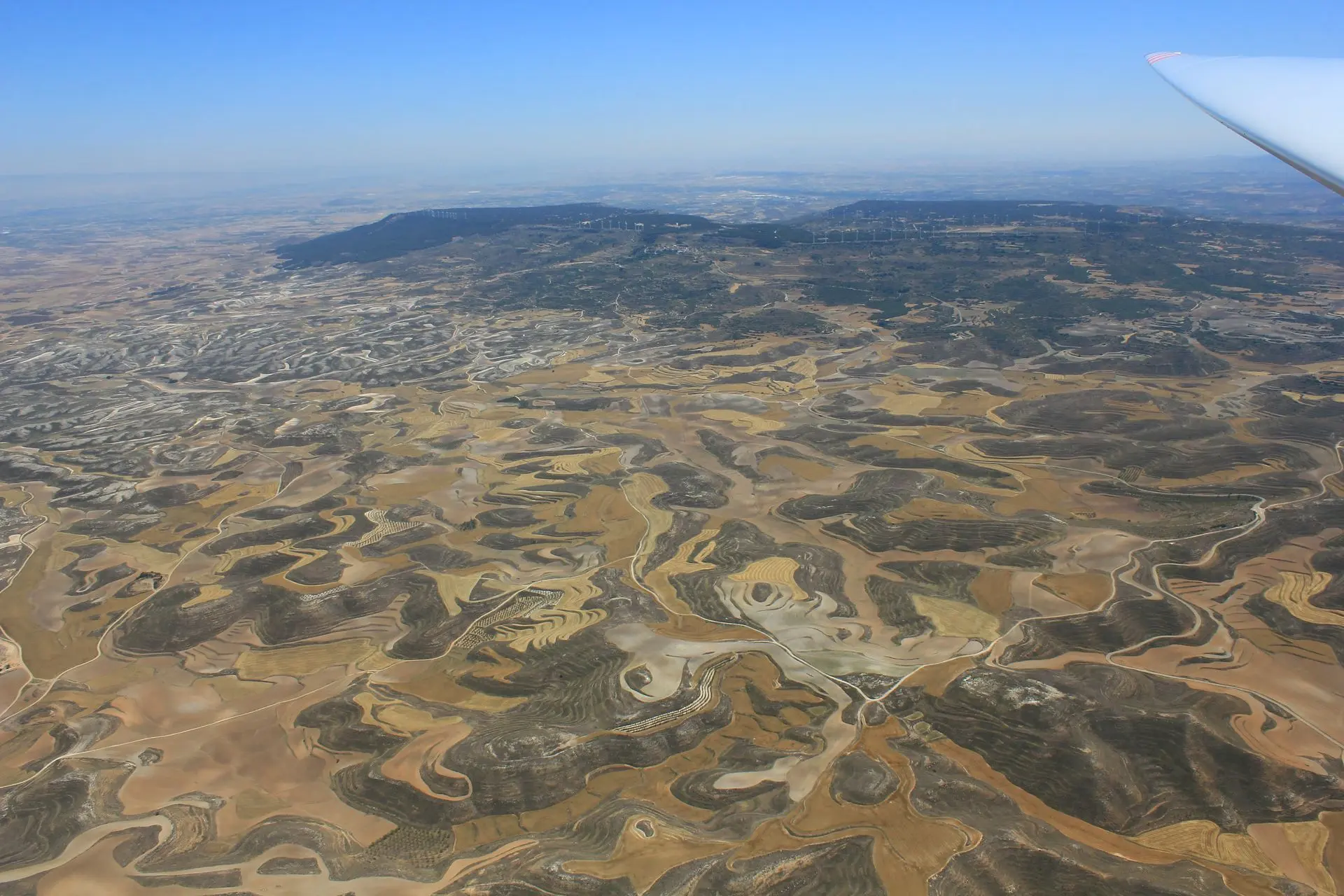 Eine Luftaufnahme: Die Landschaft ist vorwiegend braun, im Hintergrund auch dunkle Waldflächen.