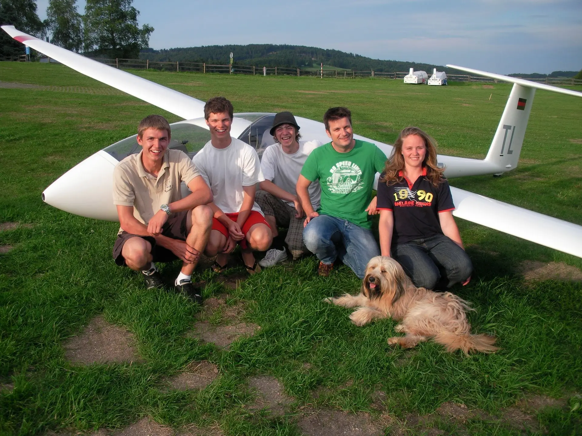 Fünf Personen und ein Hund vor einem Segelflugzeug.
