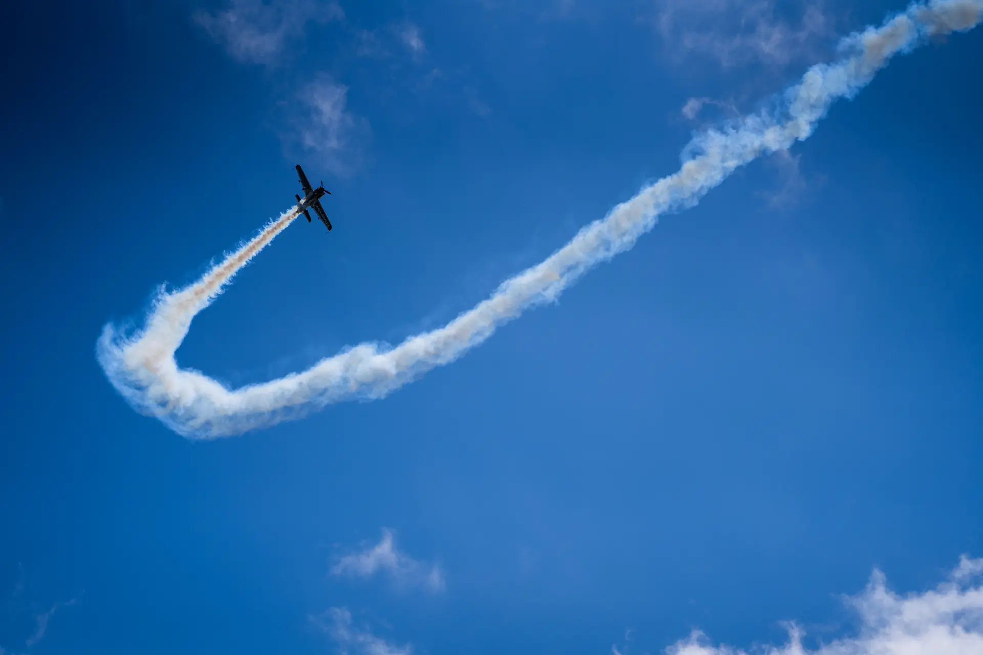 Kunstflugzeug zieht eine geschwungene Rauchspur durch den blauen Himmel